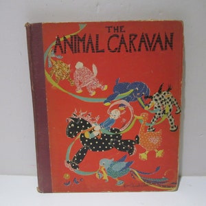 Könnte beinhalten: Der Einband eines antiken Kinderbuches mit dem Titel "The Animal Caravan". Der Einband zeigt einen roten Hintergrund mit einer Vielzahl von bunten Tieren, darunter ein Pferd, eine Ente, ein Elefant, ein Kaninchen, eine Katze und ein Vogel. Die Tiere sind alle in gepunkteten und gestreiften Kleidern gekleidet.