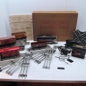 Puede incluir: Un tren de juguete vintage con una locomotora roja, negra y plateada, un vagón de cola rojo y una vía plateada. El set incluye un transformador y una vía de cambio. La caja está etiquetada "Stream Line Toy Trains Electrical Train".