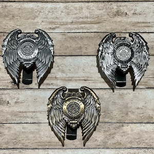 May include: Three silver and gold metal badge holders with eagle wings and a round center featuring the words "Officer St. Michael Patron Saint of Police Protect Us FLA".