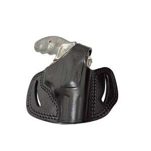 May include: A black leather holster with a silver revolver. The holster has a molded design with stitched edges and two oval cutouts. The revolver's grip is visible above the holster.