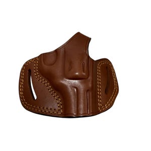 May include: A brown leather holster with visible stitching and a molded design. The holster features a curved shape with openings for a firearm. The leather has a glossy finish.