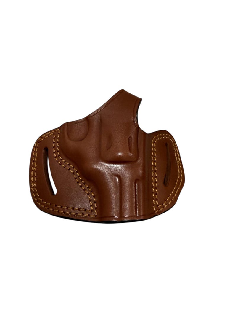 May include: A brown leather holster with visible stitching and a molded design. The holster features a curved shape with openings for a firearm. The leather has a glossy finish.