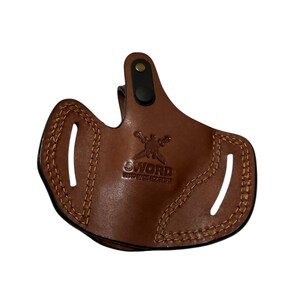 May include: A brown leather holster with the word "SWORD" embossed on the front. The holster has a stitched design around the edges and two slots. A black clip is attached to the top.