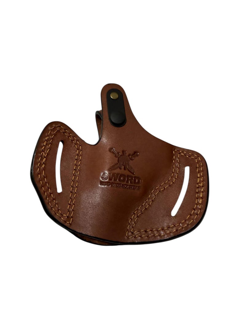 May include: A brown leather holster with the word "SWORD" embossed on the front. The holster has a stitched design around the edges and two slots. A black clip is attached to the top.