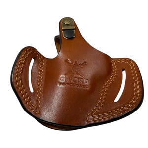 May include: A brown leather holster with visible stitching and the text "SWORD HAND MADE HOLSTERS". The holster has two oval cutouts and a metal clip. The leather is a medium brown color.