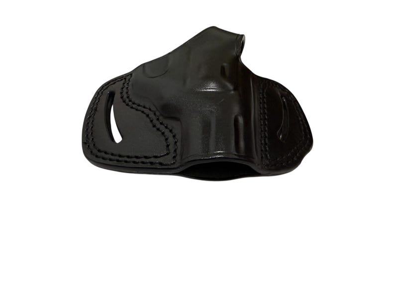 May include: A black leather holster with visible stitching and a glossy finish. The holster has a molded design with openings for a firearm. The overall shape is designed to fit a handgun.