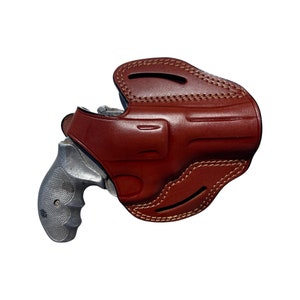 K&ouml;nnte beinhalten: Ein braunes Lederholster f&uuml;r einen Revolver. Das Holster hat eine Klappe, die den Abzugsschutz bedeckt, und eine G&uuml;rtelschlaufe.