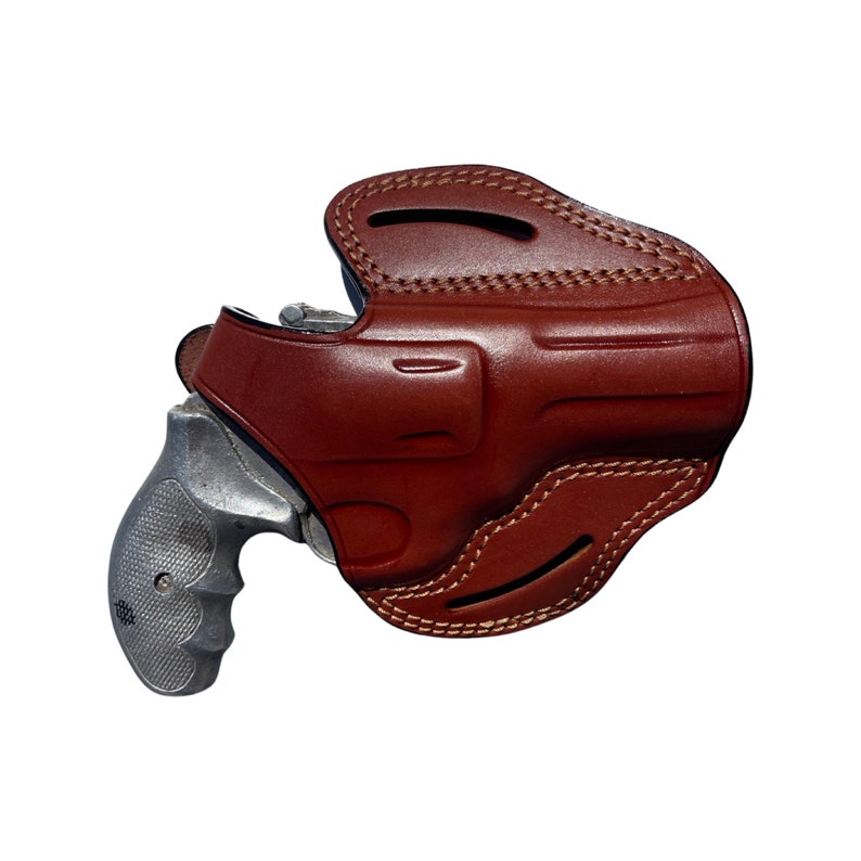 K&ouml;nnte beinhalten: Ein braunes Lederholster f&uuml;r einen Revolver. Das Holster hat eine Klappe, die den Abzugsschutz bedeckt, und eine G&uuml;rtelschlaufe.