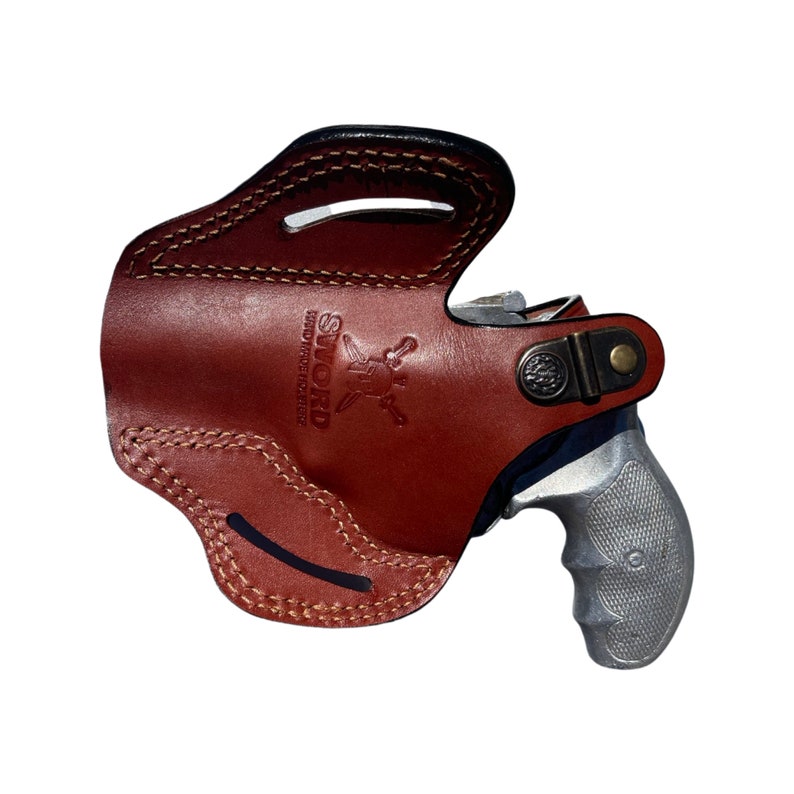 K&ouml;nnte beinhalten: Ein braunes Lederholster mit einem silbernen Revolver darin. Das Holster tr&auml;gt den Text "SWORD HANDMADE LEATHER" in Pr&auml;gung.