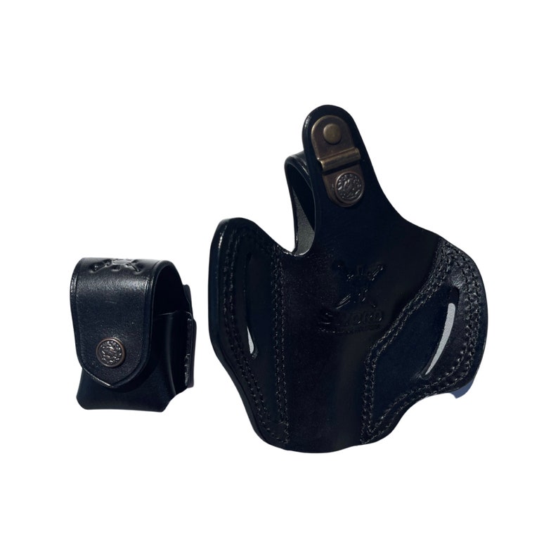 K&ouml;nnte beinhalten: Schwarzes Lederholster mit Druckknopfverschluss und einer kleineren schwarzen Ledertasche. Das Holster hat ein gen&auml;htes Design und ein Metalllogo.