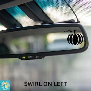 May include: A black rearview mirror with a black pumpkin sticker on the right side. The sticker has a swirl on the left side of the pumpkin.