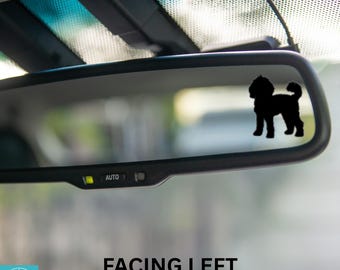 May include: A black silhouette of a dog facing left is displayed on a rearview mirror of a car. The mirror has an "AUTO" button on the bottom.