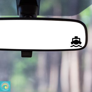 May include: A black car rearview mirror with a small black boat icon sticker on the right side of the mirror.