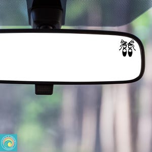 May include: A rearview mirror with a black silhouette of two ballet shoes on the glass.