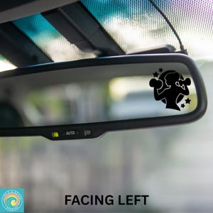 May include: Black car rearview mirror with a sticker of a woman boxing, surrounded by stars. The text "FACING LEFT" is printed at the bottom of the image. The mirror has an "AUTO" button.