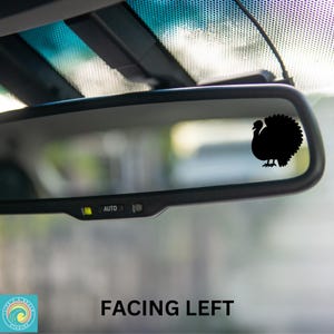 May include: A black silhouette of a turkey facing left is displayed on a rearview mirror of a car. The mirror has an "AUTO" button on the bottom.