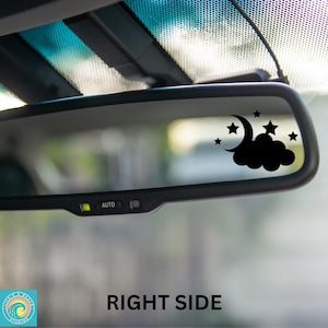 May include: A black car rearview mirror with a black crescent moon and stars sticker on the glass. The sticker is on the right side of the mirror. The mirror has an "AUTO" button.