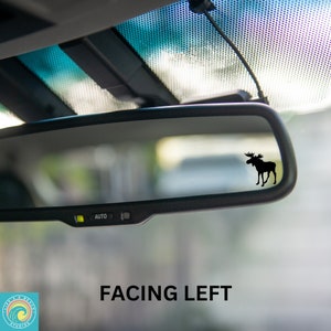 May include: A rearview mirror in a car with a black silhouette of a moose facing left. The text "FACING LEFT" is printed below the mirror.