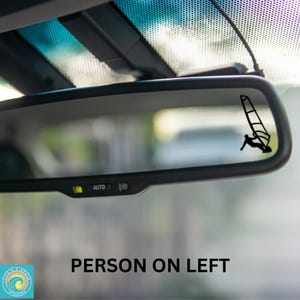 May include: A black and white silhouette of a person windsurfing, seen in the reflection of a rearview mirror in a car. The mirror has an "AUTO" button.