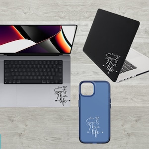 May include: A blue phone case with a white design that says "Live that Sports Mom Life" with an arrow pointing to the right. The case is on a wooden surface next to a laptop with a similar design on the back.