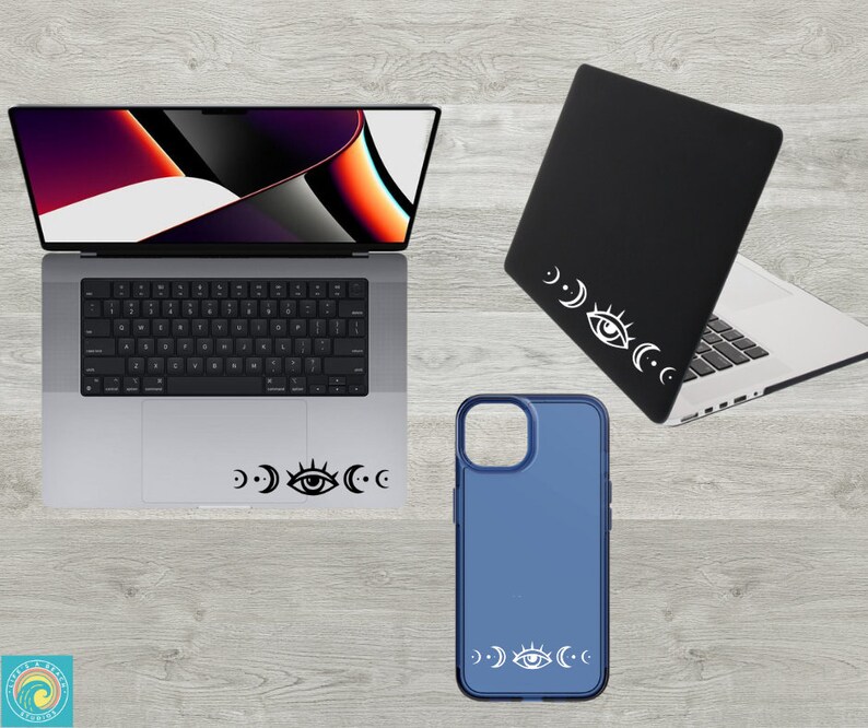 May include: A laptop, phone case, and laptop skin with a white eye and crescent moon design. The laptop is silver and has a black keyboard. The phone case is blue and the laptop skin is black.