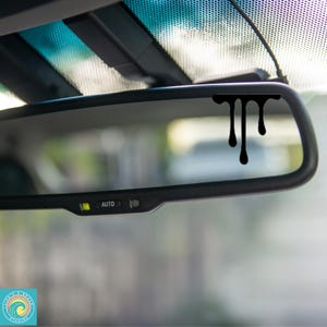 May include: A black car rearview mirror with a black dripping paint decal on the glass. The mirror has an "AUTO" button.
