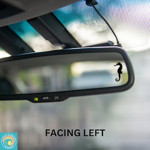May include: A black silhouette of a seahorse facing left is visible in the rearview mirror of a car. The mirror has an "AUTO" button on the bottom.