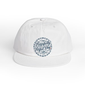 May include: White baseball cap with a curved brim. The cap features a circular design with the text "Purrfectly Perfect Day!" in a script font, surrounded by paw prints and floral accents. A small red heart is included in the design.