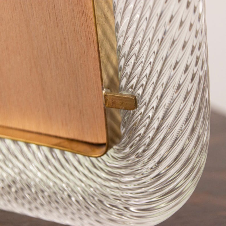 May include: A clear glass picture frame with a wood backing and a brass trim. The glass has a swirling, textured pattern.