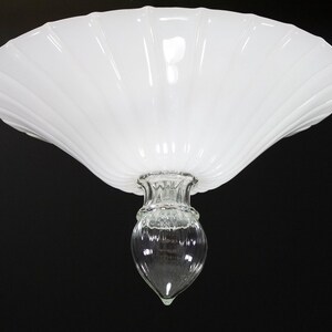 A white, scalloped-edge lamp shade with a clear glass bulb at the bottom.