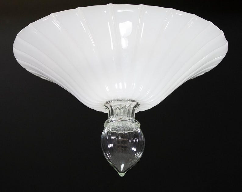 A white, scalloped-edge lamp shade with a clear glass bulb at the bottom.