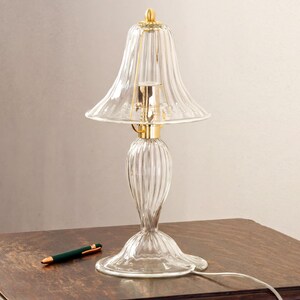 A clear glass lamp with a gold-colored base and a green pen on a wooden table.
