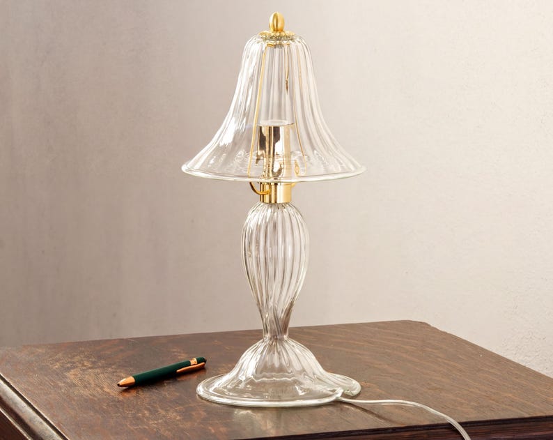 A clear glass lamp with a gold-colored base and a green pen on a wooden table.