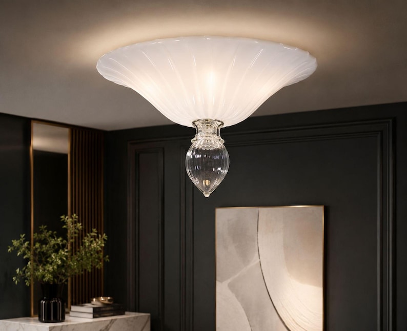a modern, elegant chandelier with a white, scalloped design hanging from the ceiling in a room with dark walls and a marble-topped table.