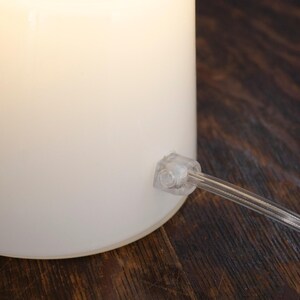 A white lamp with a clear plastic base is placed on a wooden surface.