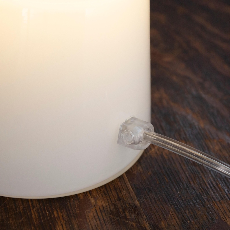 A white lamp with a clear plastic base is placed on a wooden surface.
