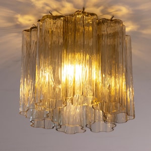 May include: A vintage ceiling light with a textured, amber glass shade. The light is on, creating a warm glow and highlighting the rippled texture of the glass. The fixture is mounted on a white ceiling.