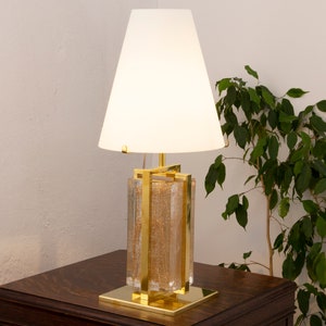 May include: A gold table lamp with a white lampshade and a clear glass base with gold accents. The base is filled with gold glitter.