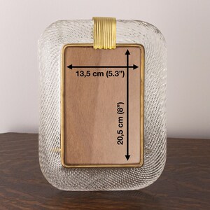 May include: A clear glass picture frame with a gold metal trim. The frame measures 8 inches by 5.3 inches.