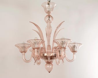 May include: A pink glass chandelier with six lights. The chandelier has a delicate, ornate design with curved arms and a central, teardrop-shaped pendant.