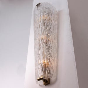 A modern wall sconce with a clear, textured design and a gold-colored base.