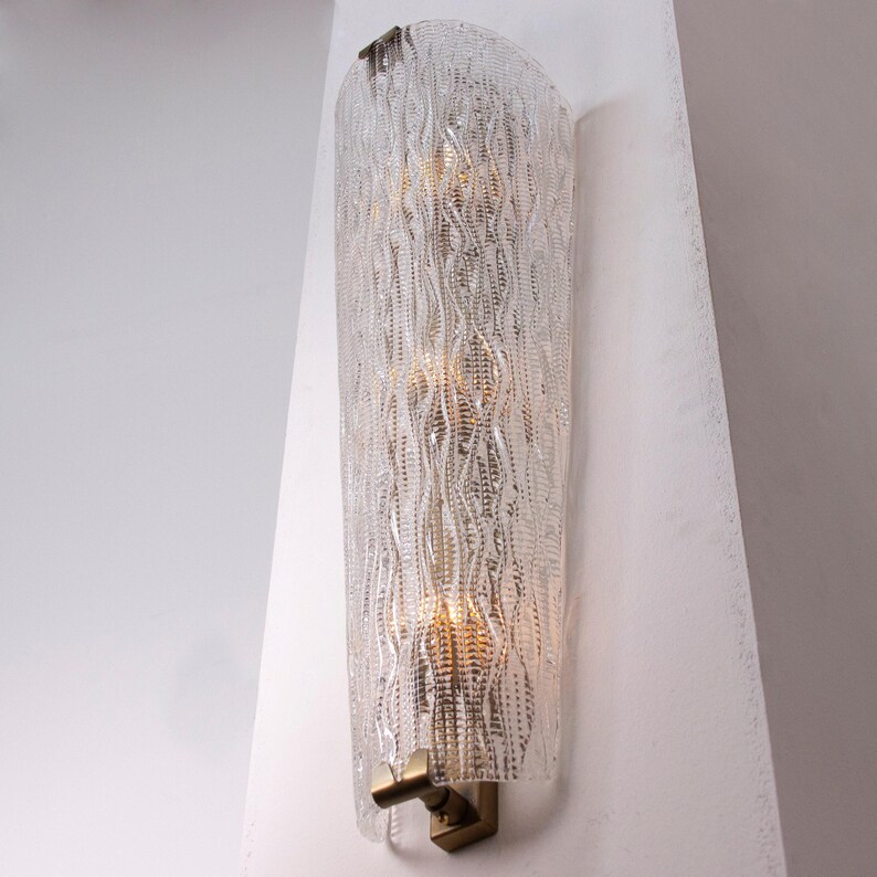 A modern wall sconce with a clear, textured design and a gold-colored base.