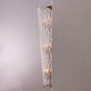 a modern, curved wall-mounted light fixture with a crystal-like design, mounted on a white wall.
