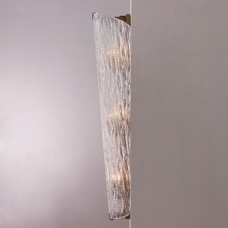 a modern, curved wall-mounted light fixture with a crystal-like design, mounted on a white wall.