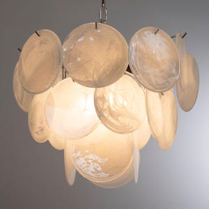 May include: A tiered chandelier featuring numerous circular, translucent white glass discs with a marbled texture. The discs are arranged in overlapping layers around a central light source, suspended from a silver-toned metal chain fixture.