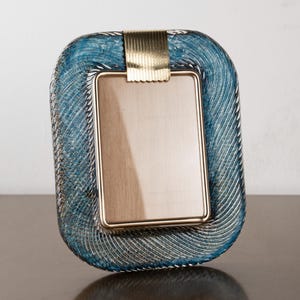 May include: A rectangular photo frame with a blue and silver woven design around the edges. The frame has a gold-coloured metal accent at the top and a gold-coloured metal frame around the photo area.