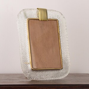 May include: A clear glass picture frame with a textured surface and a gold metal trim. The frame has a rectangular opening for a photo.
