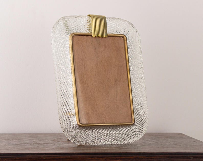 May include: A clear glass picture frame with a textured surface and a gold metal trim. The frame has a rectangular opening for a photo.