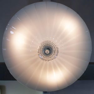 a round, white lamp with a clear glass shade, which is illuminated and casting a warm glow.
