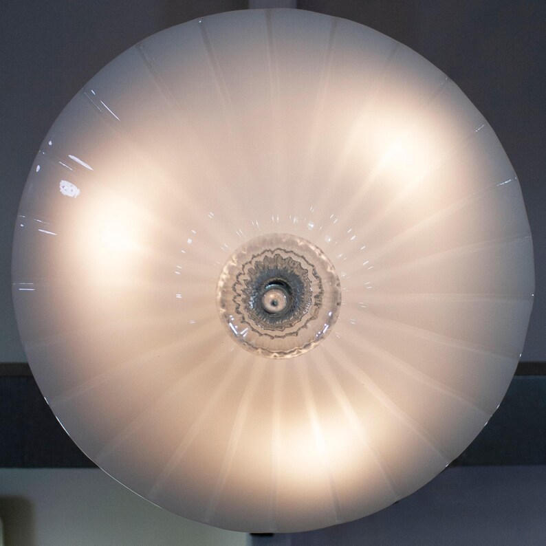 a round, white lamp with a clear glass shade, which is illuminated and casting a warm glow.